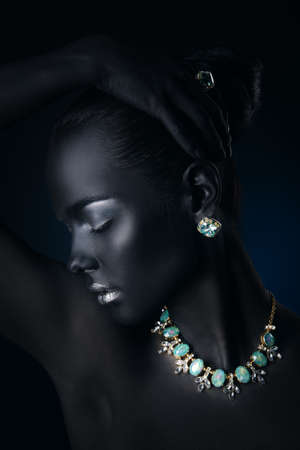 Beauty, fashion portrait. Close-up portrait of a beautiful young woman with black skin, silver glitter lips and beautiful aquamarine jewelry. Body painting project. Make-up and jewelry.の写真素材