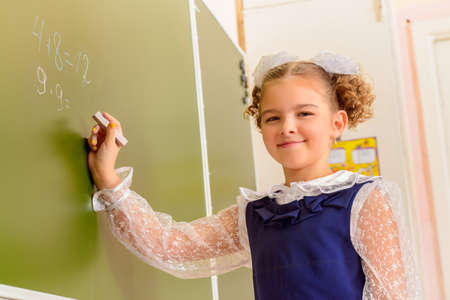 A schoolgirl in uniform writing on a blackboard. Educational concept.の写真素材