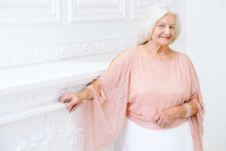 Modern well-groomed old woman with beautiful blonde hair standing in a room with a classic interior. Beauty, fashion. Luxury.の写真素材