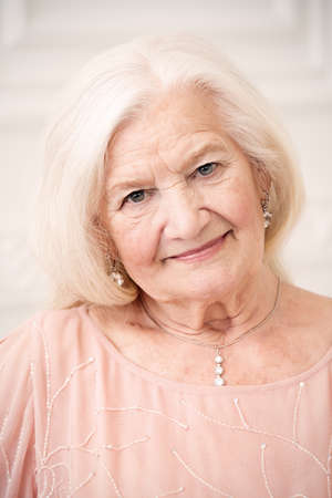 Modern well-groomed old woman with beautiful blonde hair standing in a room with a classic interior.の写真素材