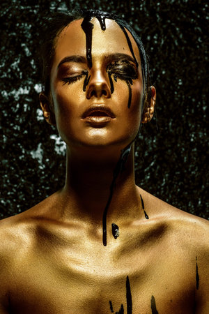 Portrait of a young woman with golden skin and black oil pouring on her.