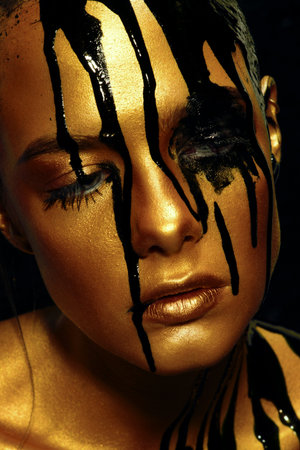 Portrait of a young woman with golden skin and black oil pouring on her.