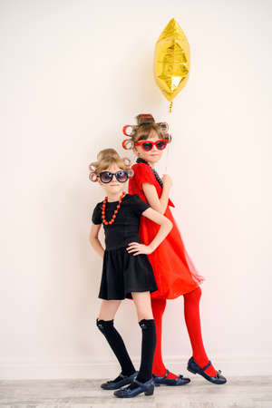 Two pretty little girls with curlers in their hair and sunglasses ready for party. Kid's fashion, beauty. Children's party, birthday.の写真素材