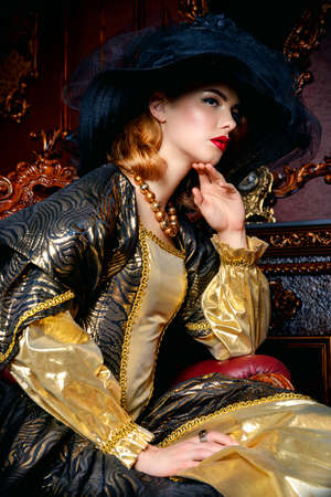 Portrait of a beautiful young woman in the lush expensive dress and elegant broad-brimmed hat in an old palace interior. Vintage style. Fashion. Renaissance Style.の写真素材