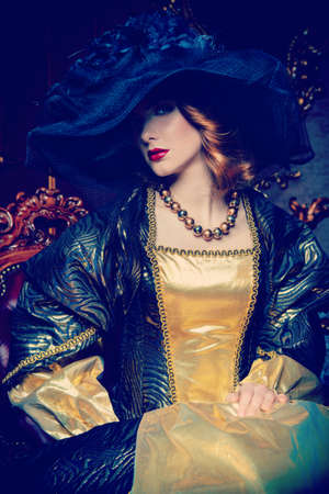 Portrait of a beautiful young woman in the lush expensive dress and elegant broad-brimmed hat in an old palace interior. Vintage style. Fashion. Renaissance Style.の写真素材