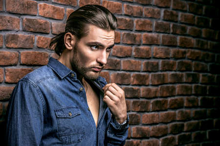 Jeans style. Portrait of a handsome young man in jeans clohes standing against the brick wall. Men's beauty, fashion. Men's barbershop, Hairstyle.の写真素材