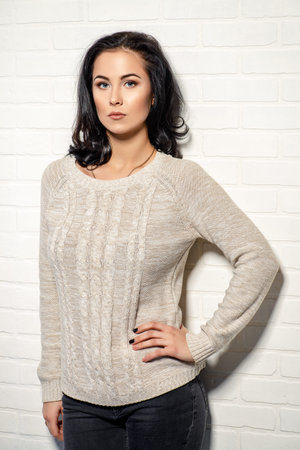 Portrait of a beautiful young woman with brunette hair posing over white brick wall. Beauty, fashion...