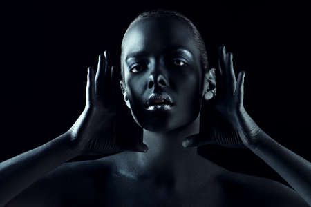 Beauty portrait. Close-up portrait of a beautiful young woman with perfect black skin and silver glitter lips. Body painting project. Cosmetics and make-up. African style.の写真素材