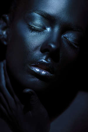 Beauty portrait. Close-up portrait of a beautiful young woman with perfect black skin and silver glitter lips. Body painting project. Cosmetics and make-up. African style.の写真素材