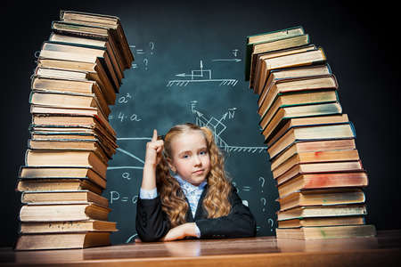 Portrait of a smart schoolgirl posing with books over school blackboard. Educational concept.の写真素材