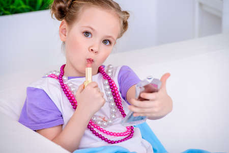 Cute little girl paints lips with mom's lipstick. Beauty, kid's fashion.の写真素材