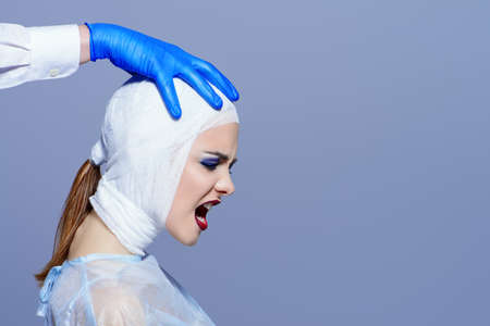 Beauty, fashion and medicine, plastic surgery. Portrait of a shouting young woman in bandages and hospital gown. Studio shot.の写真素材