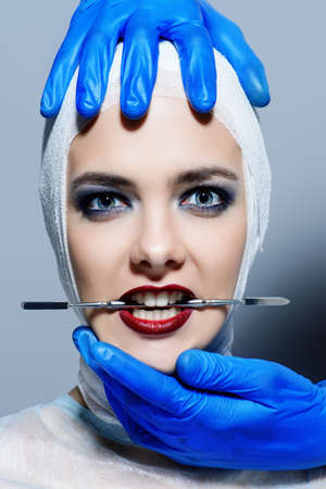 Beauty, fashion and medicine, plastic surgery. Portrait of an attractive young woman in bandages and hospital gown. Studio shot.の写真素材