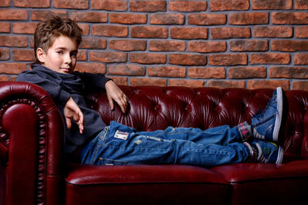 Kid's fashion. Modern nine year old boy posing at studio over brick wall background. Clothes for children.の写真素材
