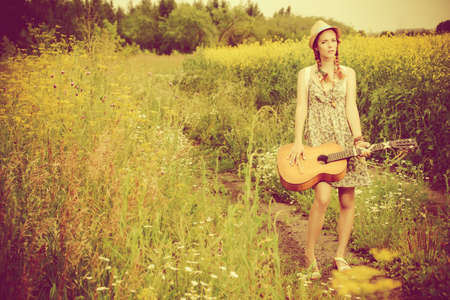 Beautiful romantic girl with a guitar on a country road on a sunny summer day.の写真素材