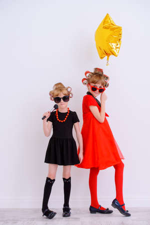 Two pretty little girls with curlers in their hair and sunglasses ready for party. Kid's fashion, beauty. Children's party, birthday.の写真素材