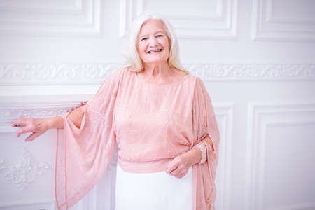 Modern well-groomed old woman with beautiful blonde hair standing in a room with a classic interior.の写真素材