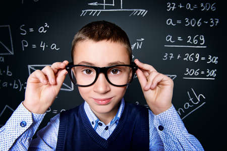 Funny smart boy in formal suit and glasses over school blackboard. Educational concept.の写真素材
