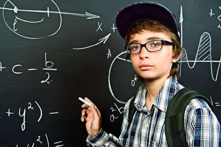 Education, high school, college. Portrait of a student boy standing by a school blackboard.の写真素材