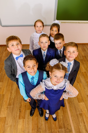 Group of happy classmates in school uniform posing together at a classroom. Education.