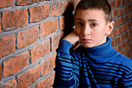 Portrait of a cute nine year old boy leaning against the brick wall.
