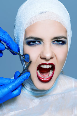 Beauty, fashion and medicine, plastic surgery. Portrait of a shouting young woman in bandages and hospital gown. Studio shot.の写真素材