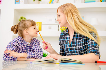 Happy family at home. Mother and daughter read and do lessons together. Education.