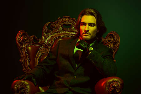 Handsome man in an expensive suit and black leather gloves sitting in a classical vintage armchair. Male beauty, fashion. Accessories.の写真素材