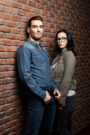 Portrait of a handsome young man and beautiful young woman standing against the brick wall. Beauty, fashion.の写真素材