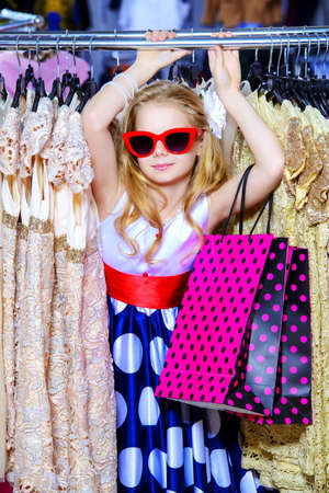 Little fashion-monger girl wearing beautiful pin-up dress and sunglasses goes shopping. Children's fashion. Sale and shopping concept.の写真素材