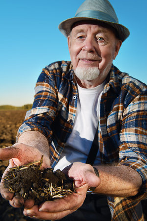 An elderly farmer holds a handful of fertile black soil in his hands and smiling. Agriculture, crop...