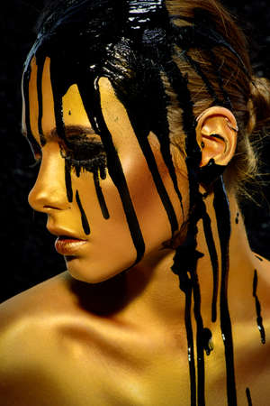 Portrait of a young woman with golden skin and black oil pouring on her.の写真素材