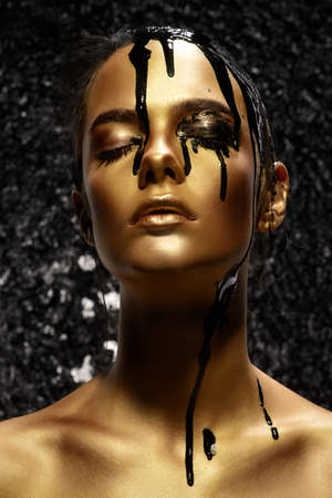 Portrait of a young woman with golden skin and black oil pouring on her.の写真素材