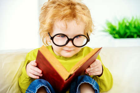 Small three year old boy in glasses is reading fairy tales. Educational concept.の写真素材