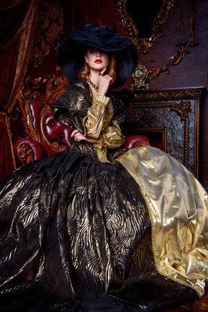 Portrait of a beautiful young woman in the lush expensive dress and elegant broad-brimmed hat in an old palace interior. Vintage style.の写真素材