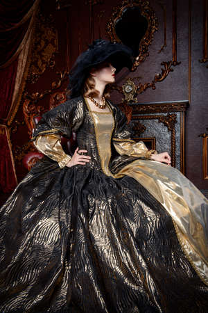 Portrait of a beautiful young woman in the lush expensive dress and elegant broad-brimmed hat in an old palace interior. Vintage style. Fashion. Renaissance Style.の写真素材