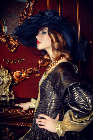 Portrait of a beautiful young woman in the lush expensive dress and elegant broad-brimmed hat in an old palace interior. Vintage style. Fashion. Renaissance Style.の写真素材