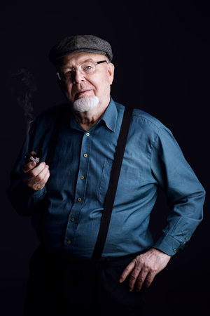 Portrait of a smiling old man smoking a pipe. Black background. Old age concept.の写真素材