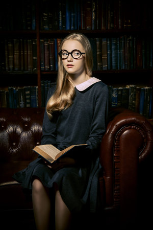 Smart student girl wearing black school dress and glasses is studying at the old library. Fairy...