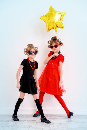 Two pretty little girls with curlers in their hair and sunglasses ready for party. Kid's fashion, beauty. Children's party, birthday.の写真素材