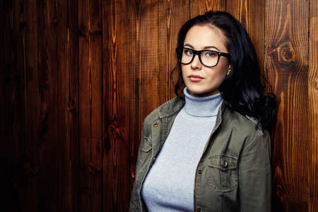 Young woman in glasses standing by the wooden wall. Business casual style. Optics.の写真素材