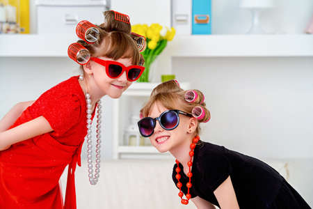 Two funny little girls with curlers in their hair are going to children's party. Kid's fashion. Family at home.の写真素材