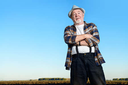 An elderly farmer standing in a plowed field. Agriculture, crop concept.の写真素材