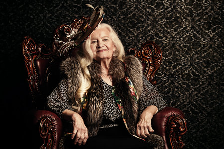 Fashionable old woman with beautiful blonde hair and elegant hat posing in vintage interior. Beauty,...