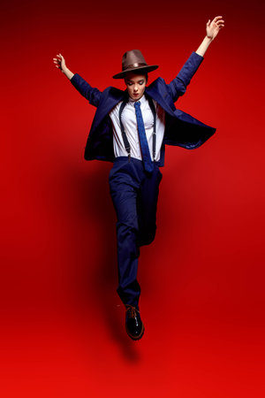 Full length portrait of an attractive young woman posing in a man's suit and a hat. Man's style clothing. Red background. Fashion shot.の写真素材
