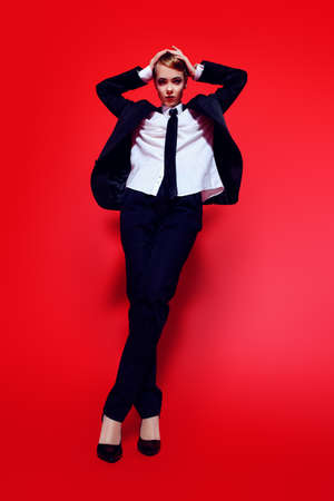 Full length portrait of an extravagant young woman posing in a man's suit. Man's style clothing. Red background. Fashion shot.の写真素材
