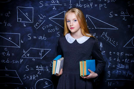 Education. Smart student girl wearing black school dress standing by a blackboard. Chalkboard background.の写真素材