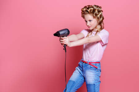 Portrait of a pretty girl teenager with curlers in her blonde hair holding hair dryer. Teen style, fashionable teen girl. Studio shot over pink background.の写真素材