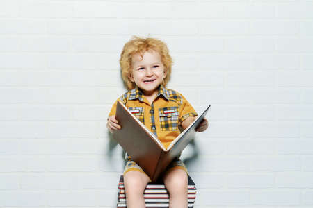 Cute little boy sitting on a stack of books with opened book. Educational concept.の写真素材