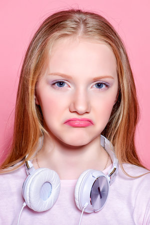 Portrait of a funny displeased girl teenager with headphones over pink background.